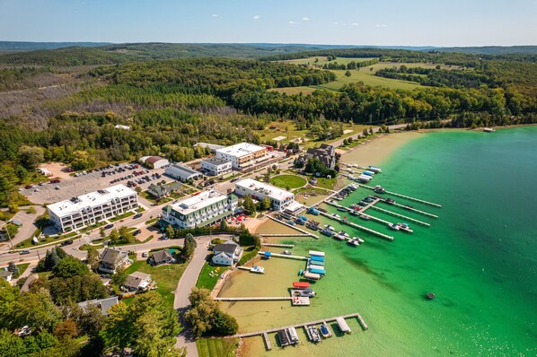 An aerial view of a coastal area with a marina, buildings, and a forested landscape.