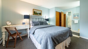 A bedroom with a bed, desk, chair, and a door leading to a bathroom.