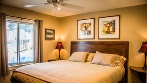 A bedroom with a large bed, two bedside tables, a ceiling fan, and two framed pictures on the wall.