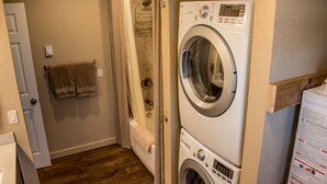 A laundry room with a front-loading washing machine, a shower, and a towel rack with towels.