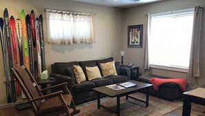 A living room with a sofa, a rocking chair, a coffee table, and skis on the wall.