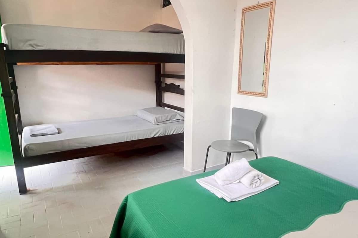 Una habitación con literas, una colcha verde, una mesita redonda y un espejo en la pared.