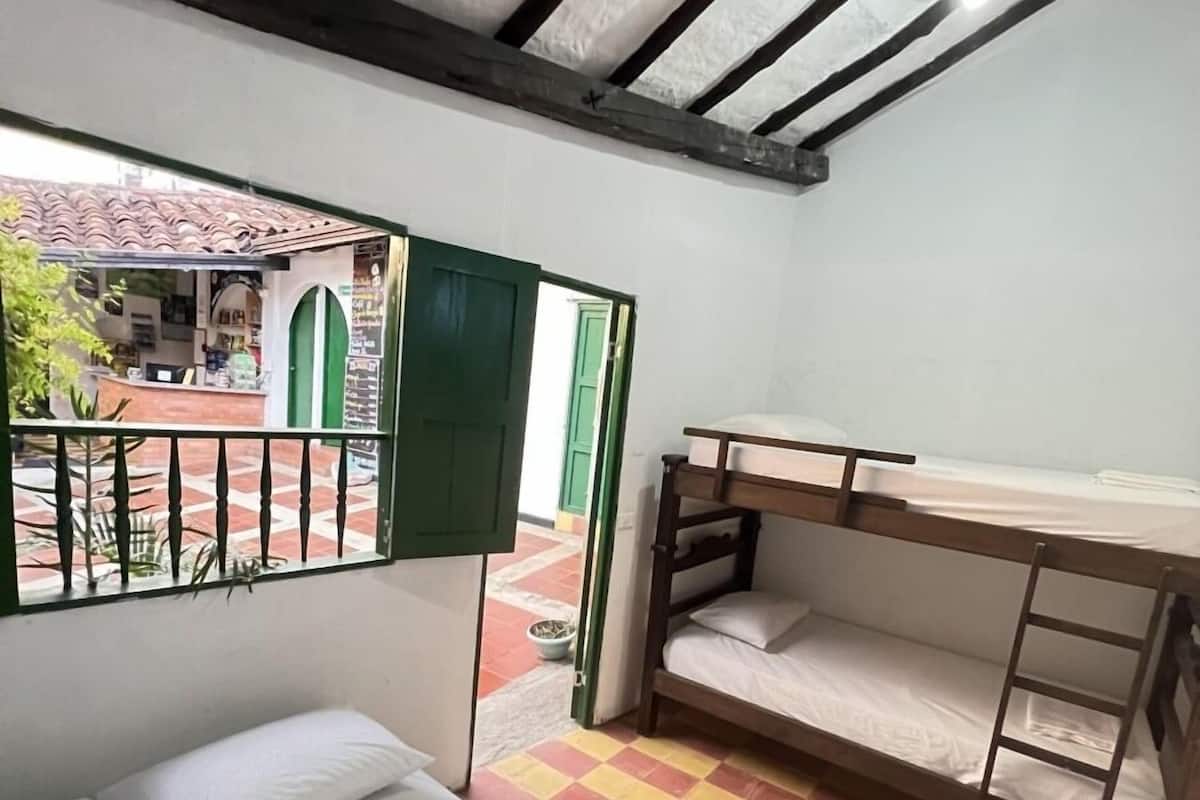 Una habitación con una cama, una litera, un escritorio y vistas a un espacio exterior con piso de baldosas y una puerta verde.