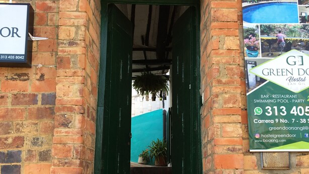 A brick building with a green door and a signboard advertising a hostel. - Green Door Hostal San Gil - Hostel (San Gil)