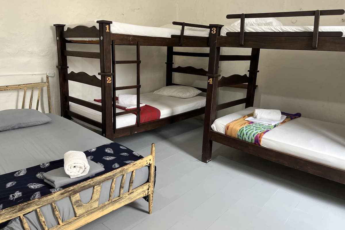 Un dormitorio con cuatro literas, cada una con una etiqueta numérica, una cama individual con una colcha estampada y una silla de madera.