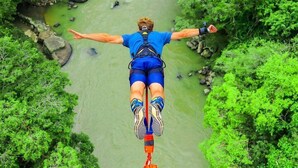 A person bungee jumping with arms outstretched over a river surrounded by greenery. - Green Door Hostal San Gil - Hostel (San Gil)