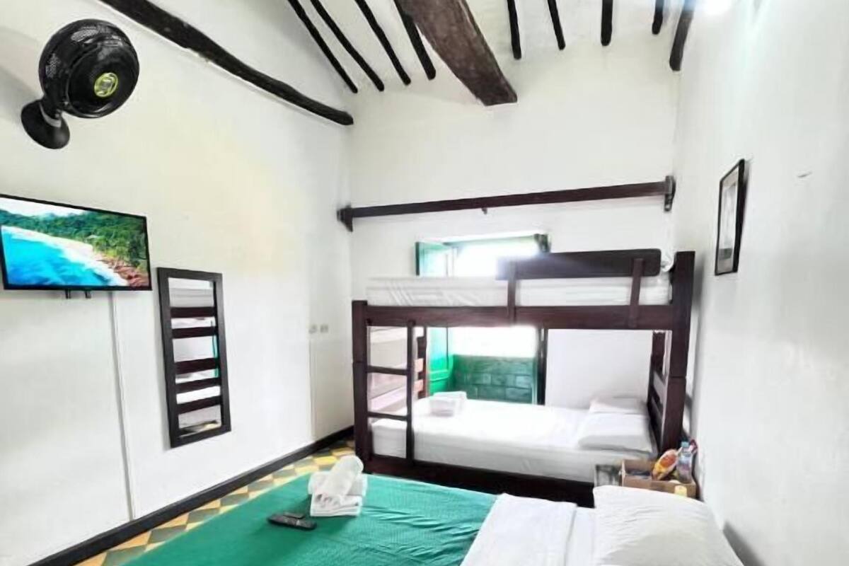 Una habitación con literas, una colcha verde, una colcha blanca, un televisor y un cuadro en la pared.