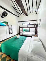 Una habitación con literas, una colcha verde, una colcha blanca, un televisor y un cuadro en la pared.