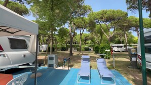Un terrain de camping avec des emplacements pour camping-cars, un espace détente bleu et des arbres.