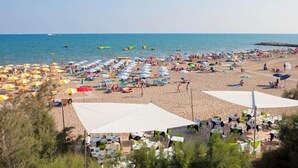Une plage avec de nombreux parasols et des chaises, une zone sablonneuse avec des tables et des chaises, et une vue sur la mer.