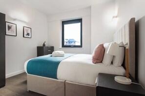 A modern bedroom with a bed, bedside table, and a window.
