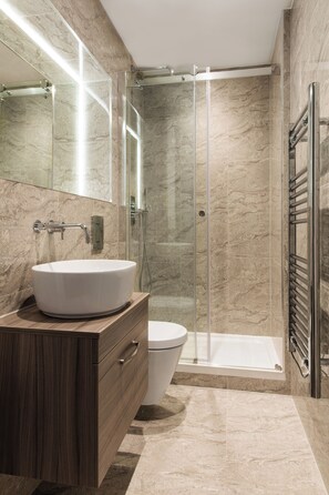 A modern bathroom with a large white sink, a glass-enclosed shower, and a toilet.