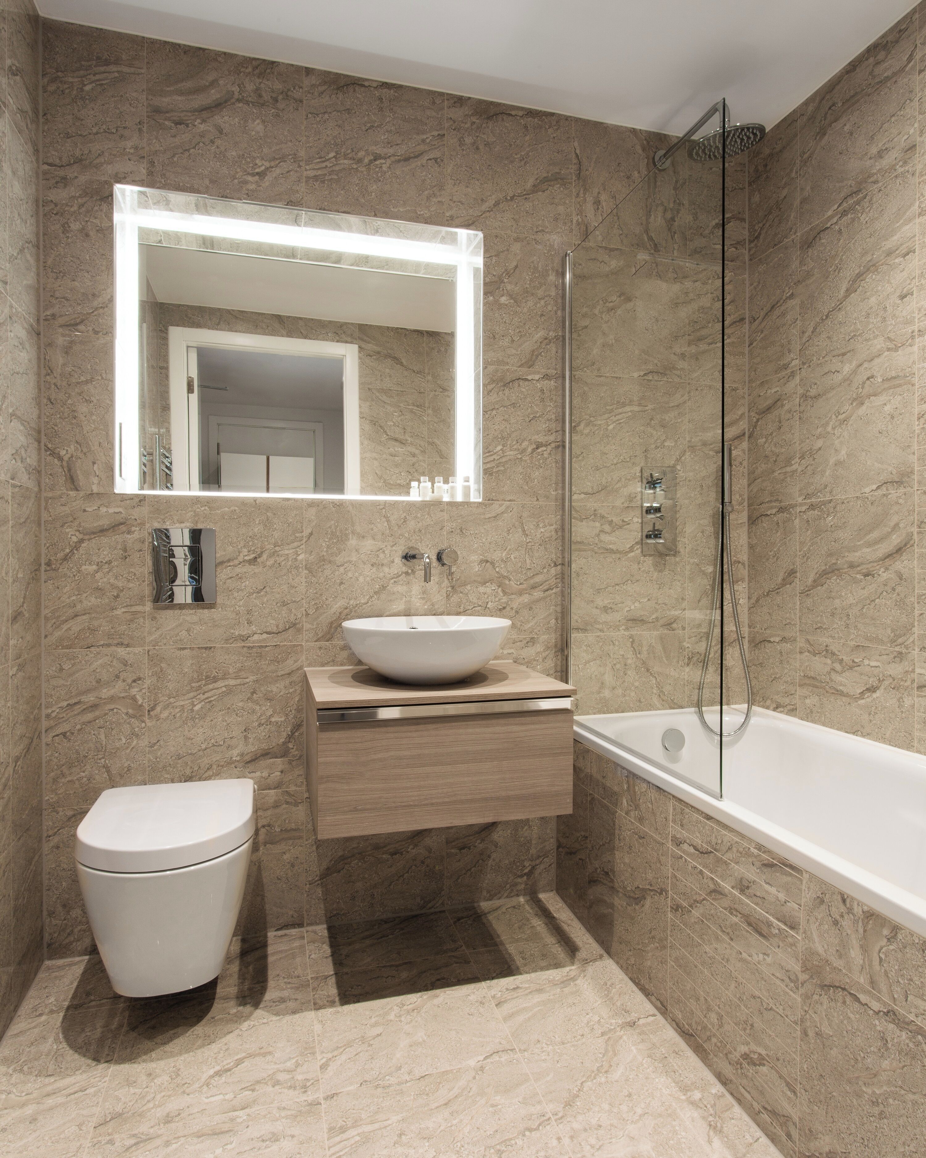 Une salle de bain moderne avec un mur en marbre, un lavabo blanc, des toilettes et une baignoire.