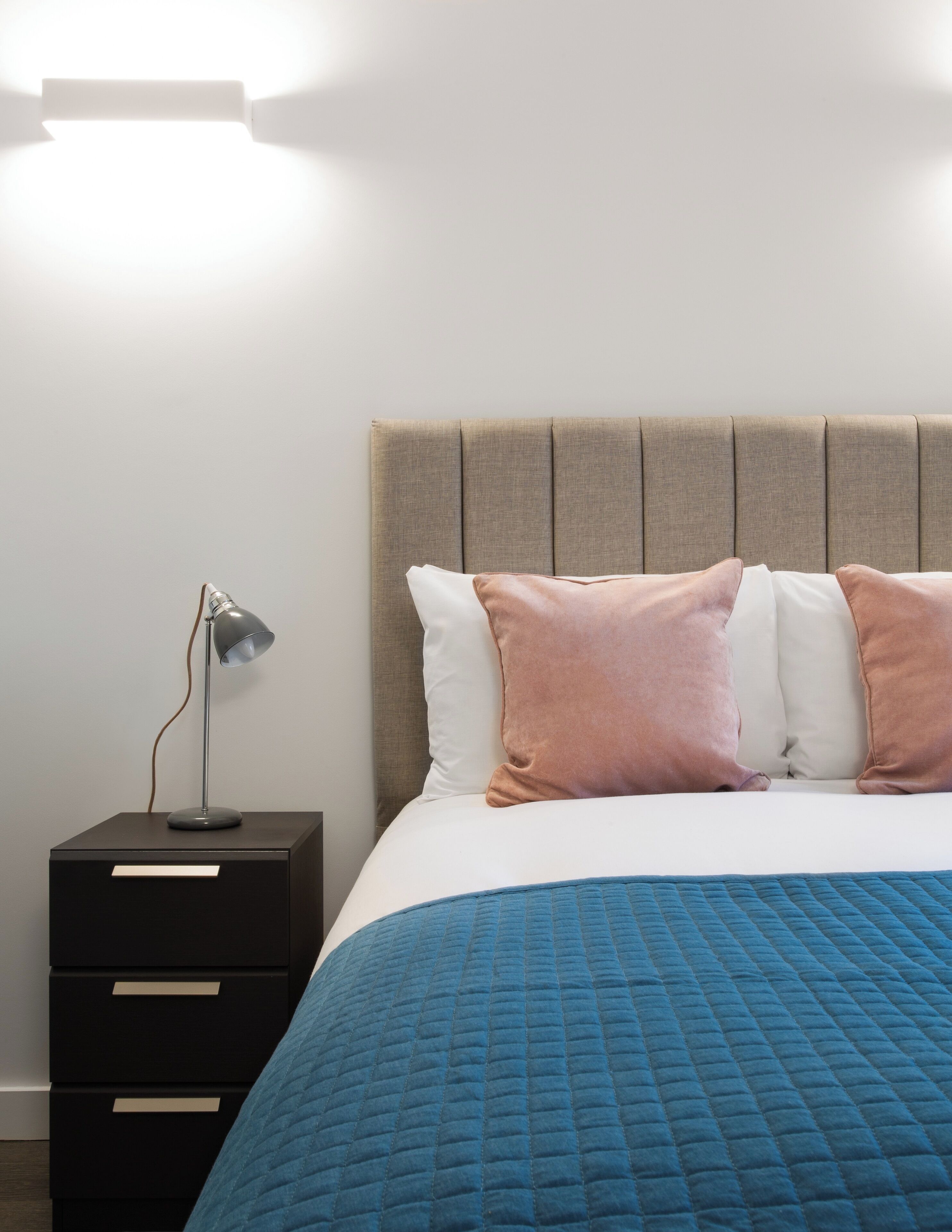 A neatly made bed with a blue quilt, a headboard, and two bedside lamps.