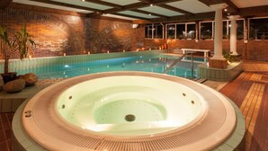 Zona d'spa amb un bany d'hidromassatge, una piscina i una paret de maó amb disseny d'arcs.