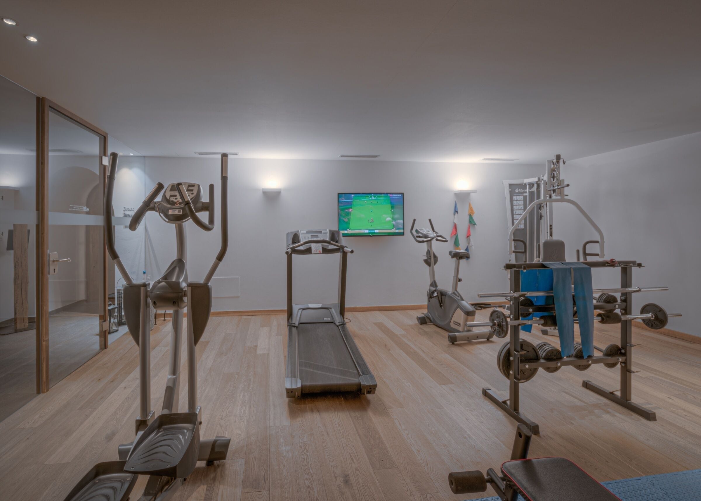 A gym with cardio machines, weightlifting equipment, and a TV screen.