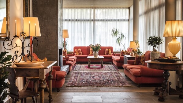 A spacious living room with a red sofa set, a coffee table, and a large window with sheer curtains.