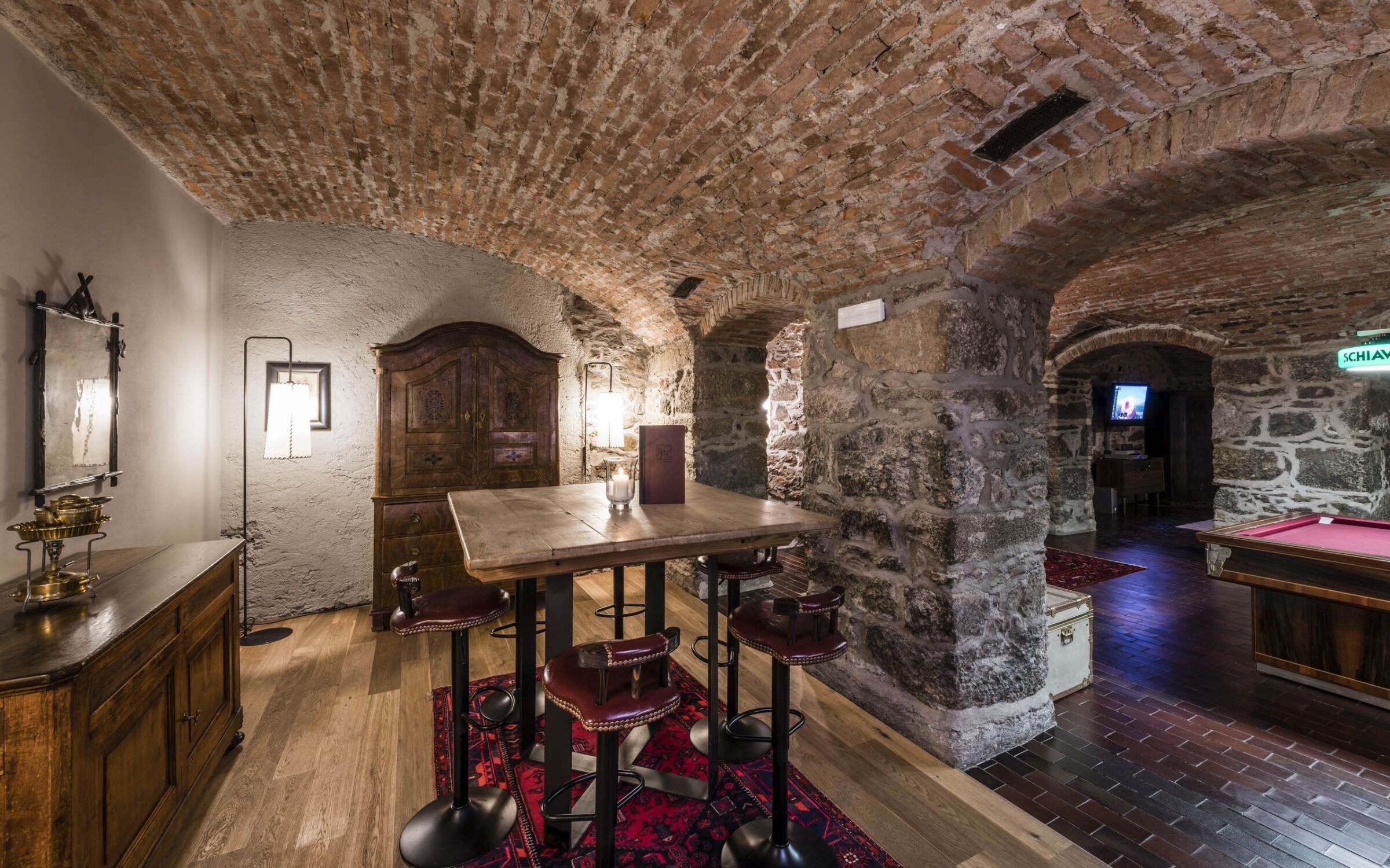 Une pièce avec une table en bois, des tabourets de bar, un miroir et un téléviseur à l’arrière-plan.