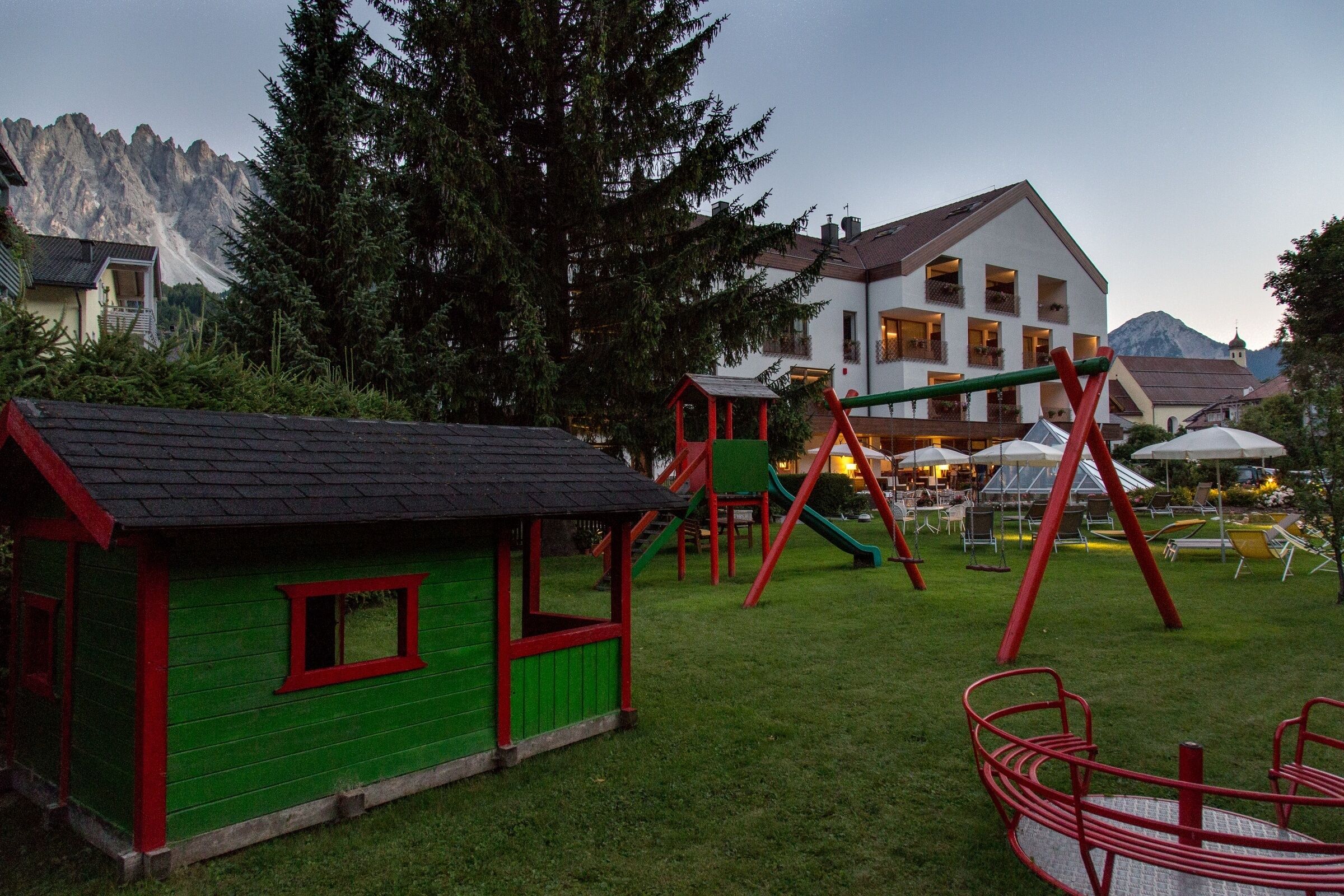 Un terrain de jeux avec des balançoires et des toboggans, une petite maisonnette verte et, au fond, un bâtiment doté de nombreuses fenêtres et de balcons.