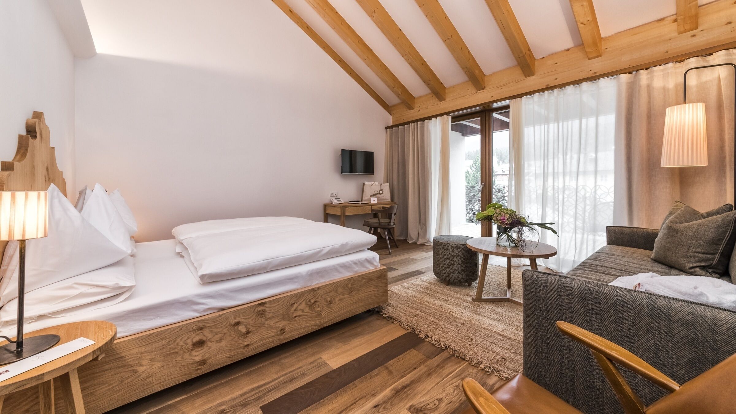 Una stanza con un letto in legno, un divano, un tavolino, una televisione e una finestra con tende.