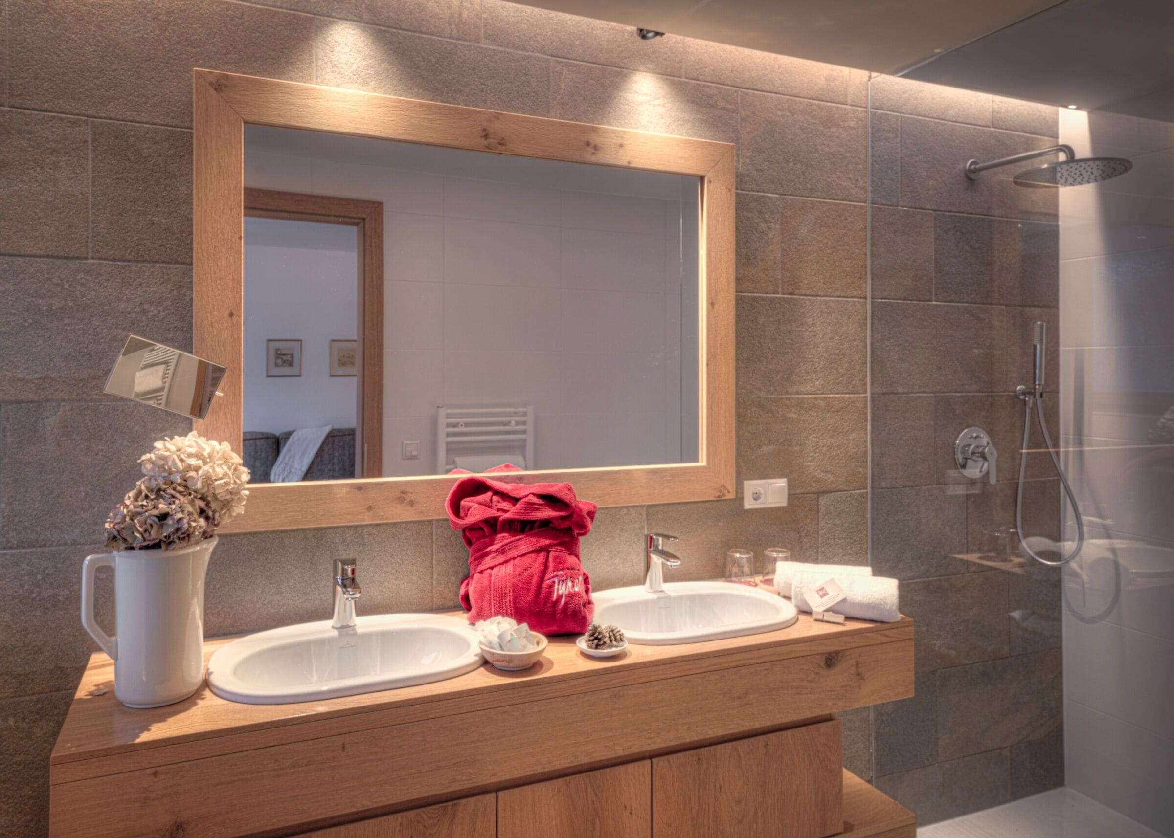 Un baño con tocador de madera, dos lavamanos, un espejo grande y zona de ducha.