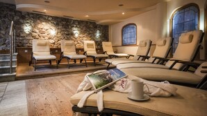 Una sala de spa amb diverses cadires reclinables, una paret de pedra, una finestra i un llit de massatge amb tovalloles i un llibre.