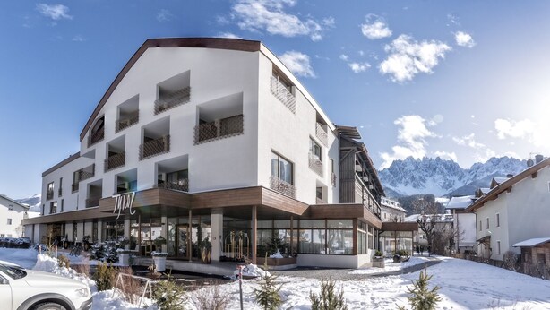 Un hotel modern amb façana blanca, diversos balcons amb baranes metàl·liques i un paisatge de zona d'esquí al fons.