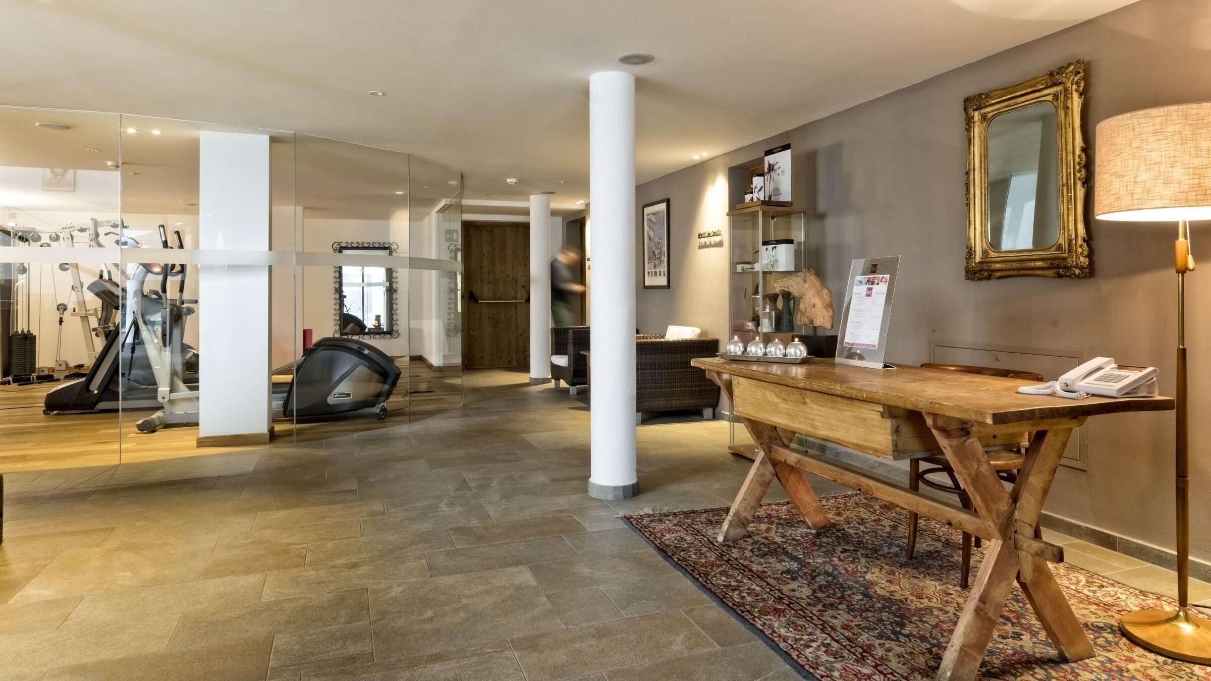 A spacious hotel lobby with a reception desk, a mirror, and a fitness area with exercise equipment.