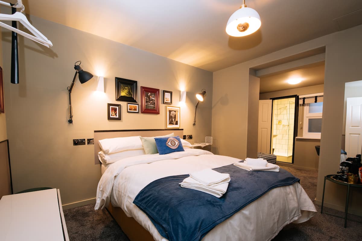 A neatly made bed with a blue blanket, a bedside table with a lamp, and framed pictures on the wall.