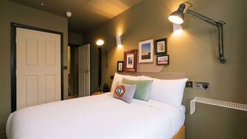 A neatly made bed with a pillow, a wall-mounted lamp, and a door to the left.