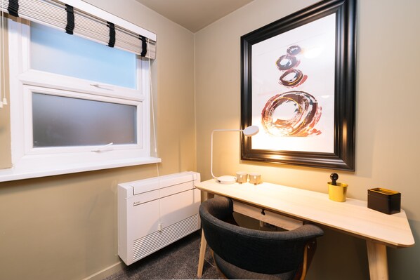 A small, well-lit room with a desk, chair, radiator, and a framed artwork on the wall. -  The Warwick by Nestor (London)