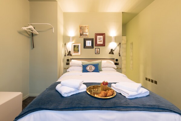 A neatly made bed with a tray of croissants and a cup of coffee, towels folded on the bed, and a wall-mounted towel rack. - The Warwick by Nestor (London)