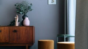 A modern room with a wooden cabinet, a pink vase with flowers, and two round ottomans. -  The Warwick by Nestor (London)