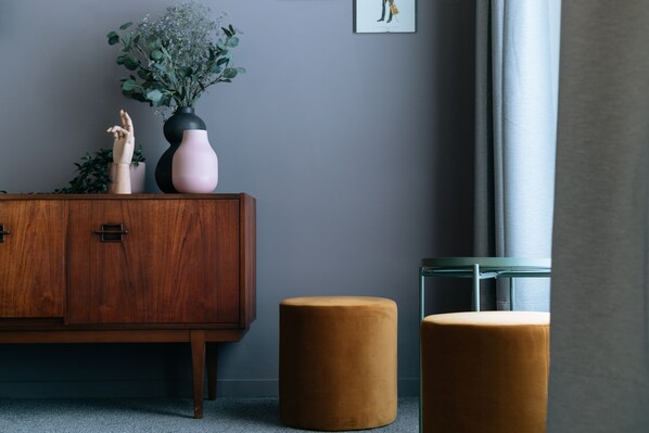 A modern room with a wooden cabinet, a pink vase with flowers, and two round ottomans.