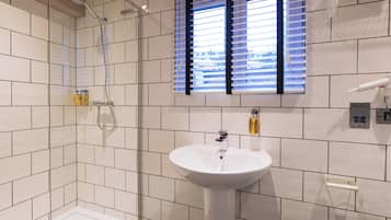 A bathroom with a shower, a sink, and a window with blinds.