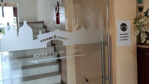 Entrada de hotel con puerta de vidrio, escalera que conduce al piso superior y cartel que indica 'aprise - open - abierto' para la entrada.