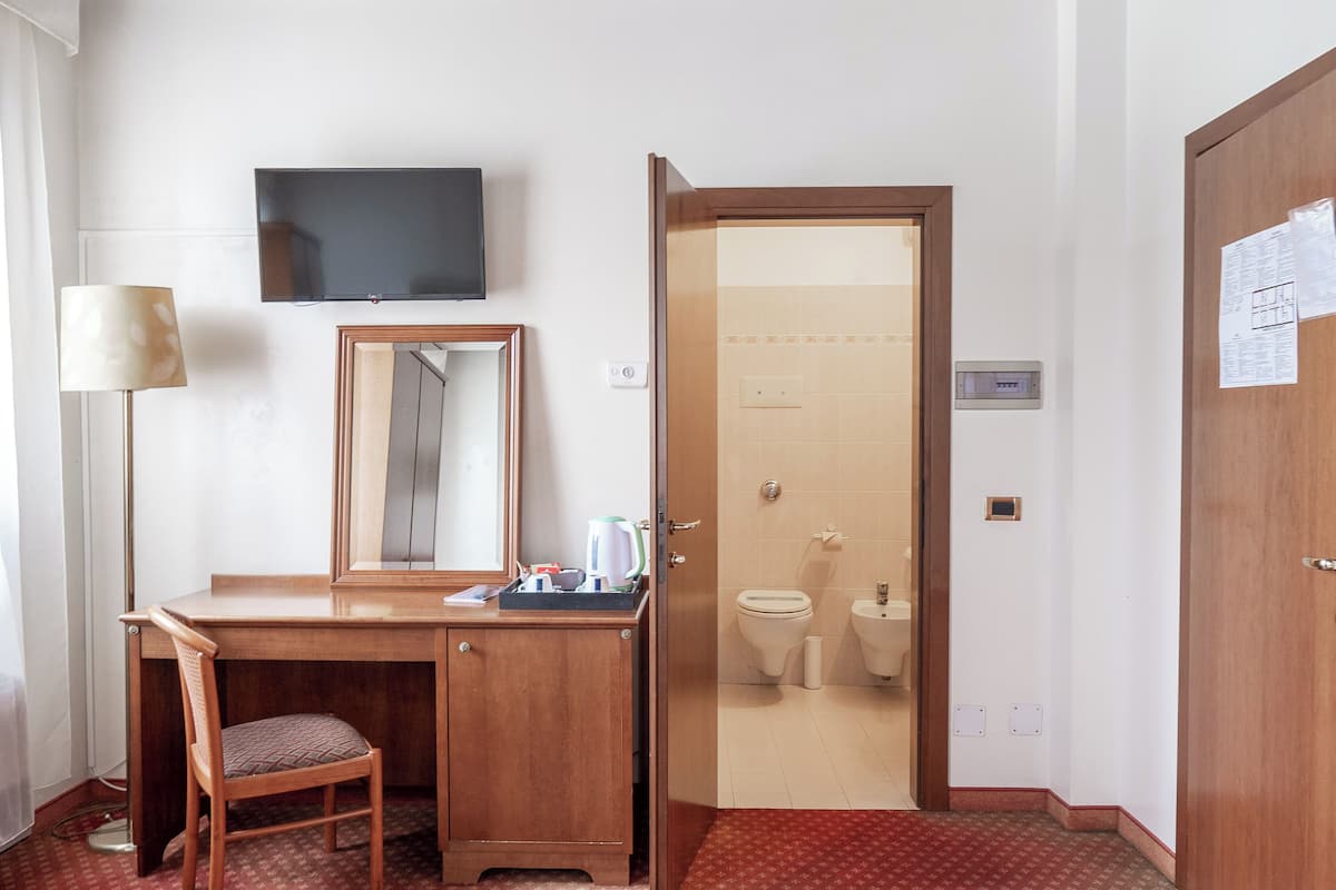 A hotel room with a wooden desk, a chair, a flat-screen TV, a mirror, and a bathroom visible through an open door.