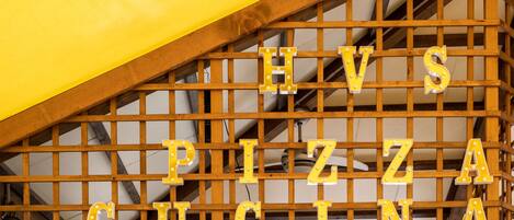 Een houten constructie met de woorden 'HV'S PIZZA CU CINA' in verlichte letters.