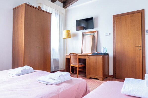 Habitación de hotel con dos camas, un escritorio, una silla, un televisor y un armario.