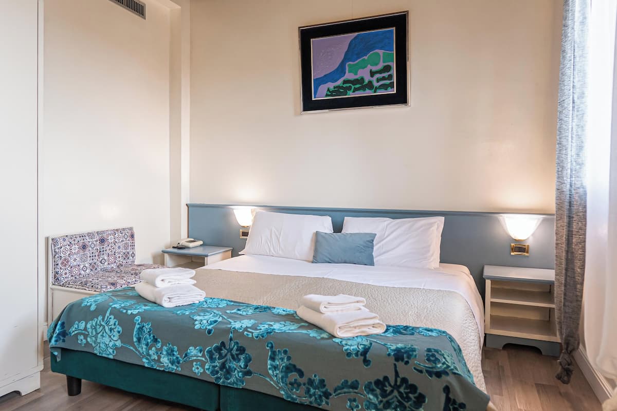 A neatly made bed with a floral bedspread, a bedside table with a lamp, and a framed artwork on the wall.