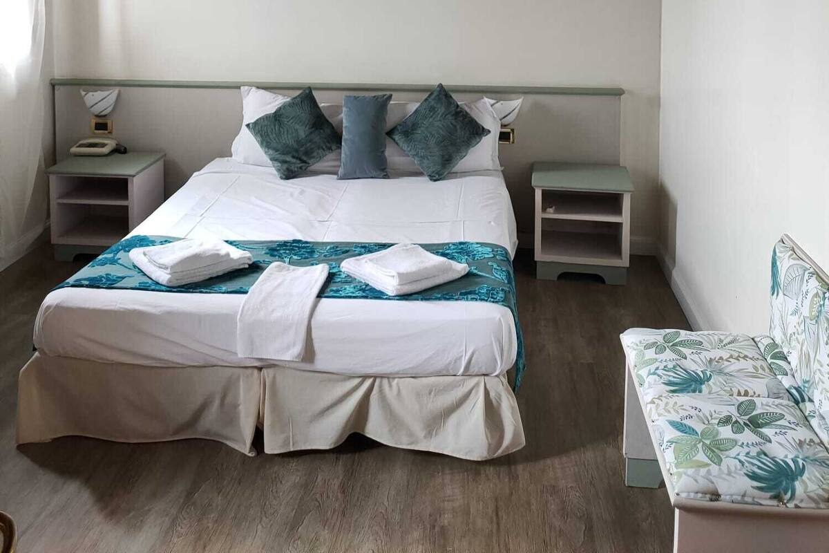 A bedroom with a bed, bedside tables, a nightstand, a chair, and a painting on the wall.