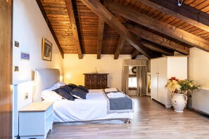 Un dormitorio con techo de madera, una cama con ropa de cama blanca, una mesita de noche, un aparador y un florero con flores.