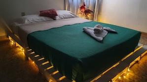Una cama con un edredón verde, almohadas blancas y una toalla enrollada encima.