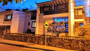 Un edificio de dos pisos con un muro de piedra en primer plano, una señal de calle y un árbol con flores.