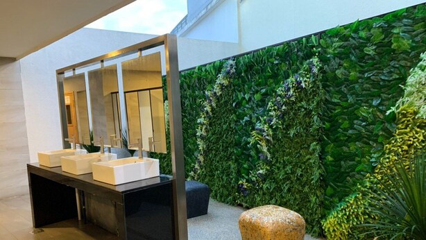A modern bathroom with a black sink counter, a mirror, and a green vertical garden wall.