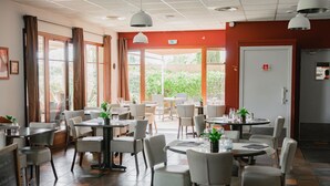 A restaurant with multiple tables and chairs, large windows, and a red wall. - Le Mas De Gaujac (Lezignan-Corbieres)