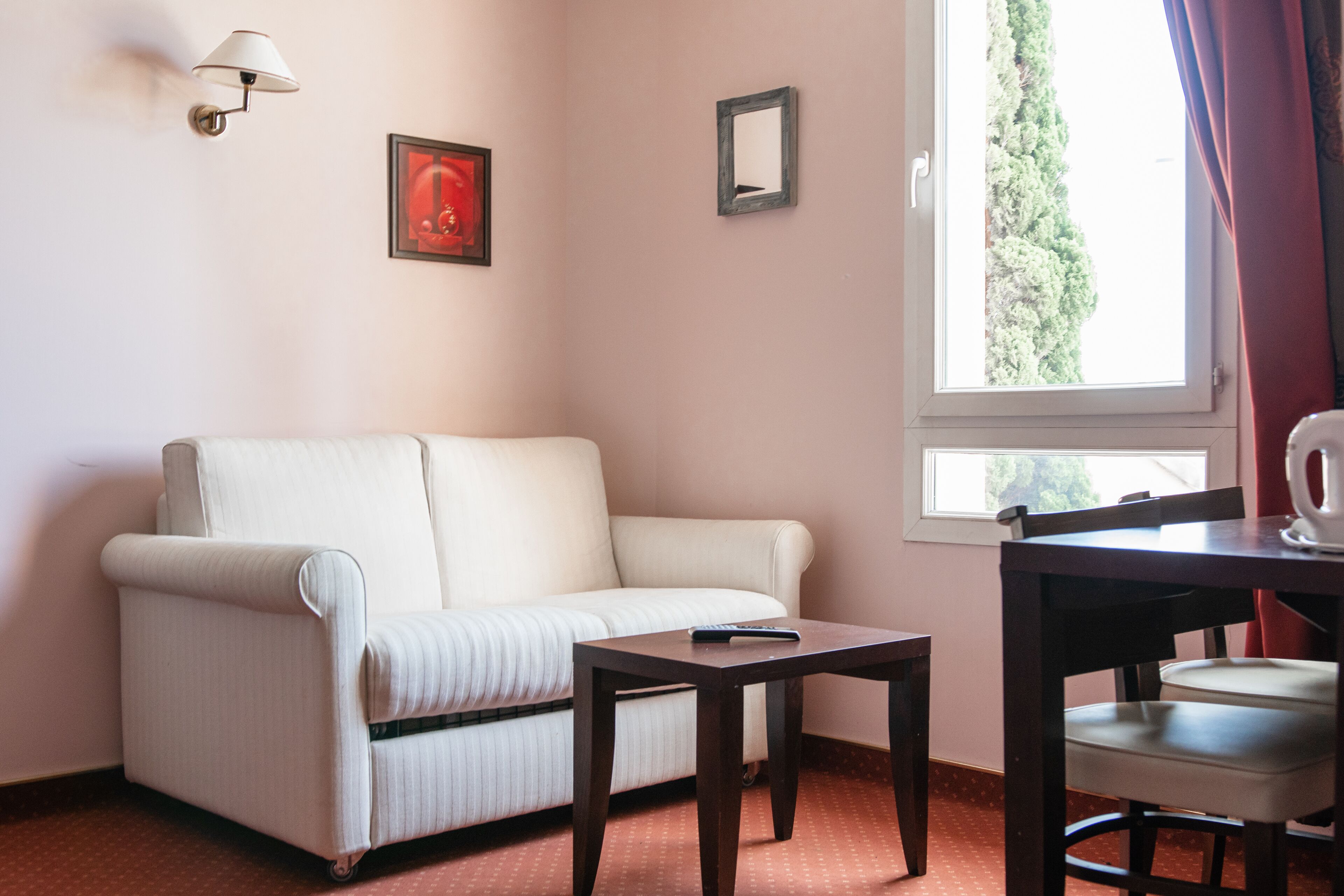 Una habitación con un sofá blanco, una mesita, una silla, una lámpara y una ventana con cortinas.