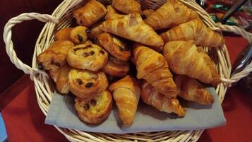 A basket of assorted pastries, including croissants and rolls, placed on a table.