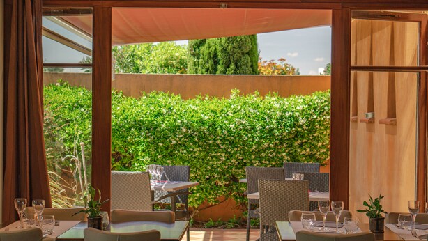 An outdoor dining area with tables and chairs, a potted plant, and a wooden door. - Le Mas De Gaujac (Lezignan-Corbieres)