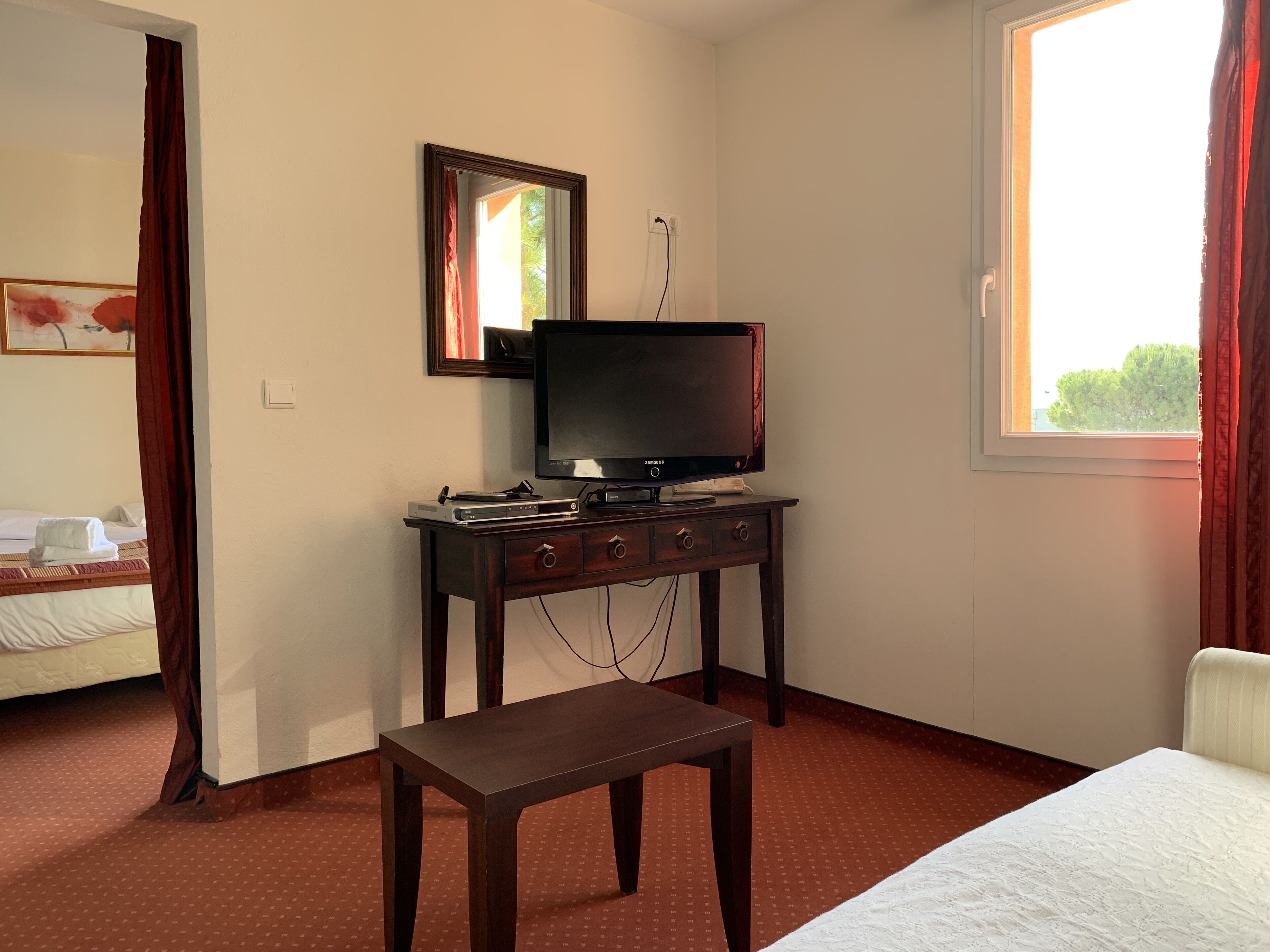 A hotel room with a bed, a desk with a television, and a window.